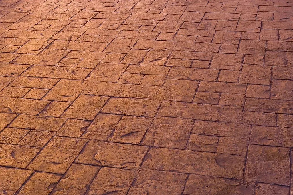 The textured surface of brown cobblestone pavement in Pompano Beach, FL, displays an intricate and uneven pattern of square and rectangular stones. Capturing various shades and shadows, it enhances the rugged appearance, ideal for residential and commercial properties seeking cost-effective concrete solutions.