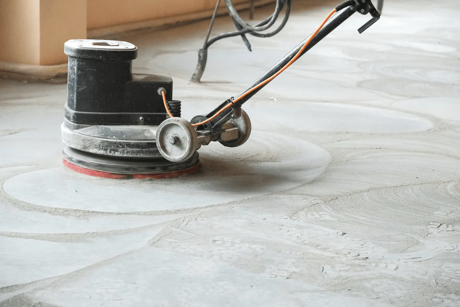 A floor polishing machine smooths a concrete surface at Lauderdale Concrete in Pembroke Pines, FL. The machine has a round base and an attached handle with cords running from it. The floor shows swirling patterns from the polishing process, creating a clean and finished look.